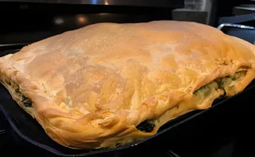 A golden layered byrek in a rectangular black cast-iron pan, with the spinach filling showing at the edges