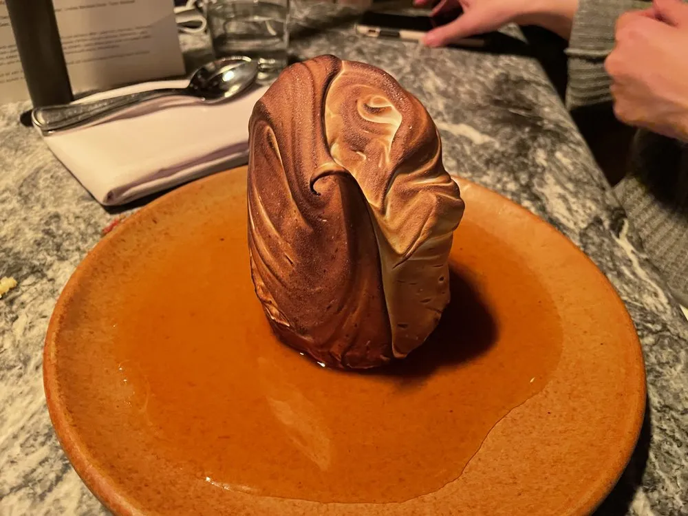 Oleana’s baked Alaska, a tall torched meringue standing in a pool of golden caramel sauce on an orange plate