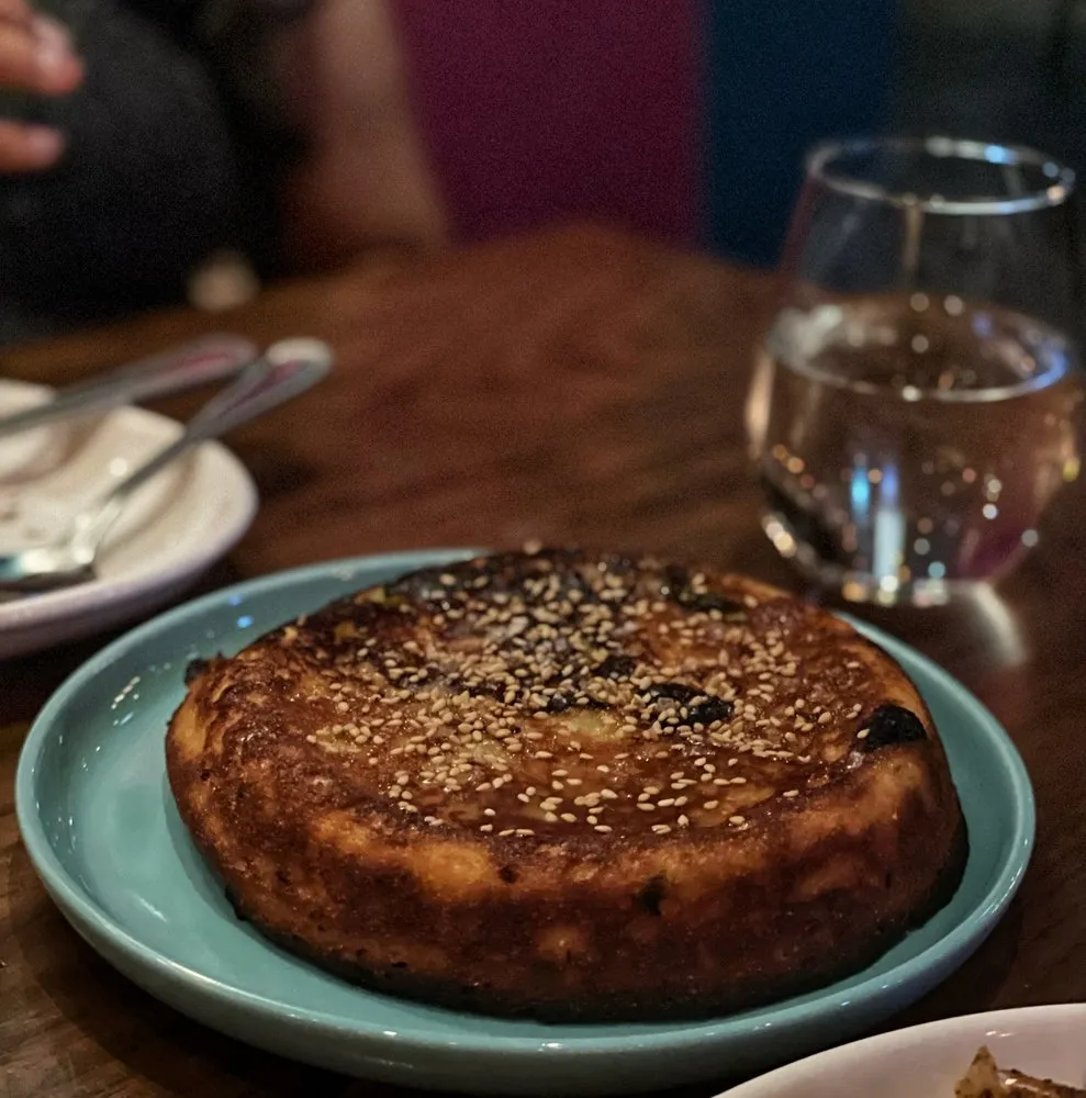 Black Sea cornbread at Sarma, a round loaf with a dark, glossy crust topped with sesame seeds, on a blue plate