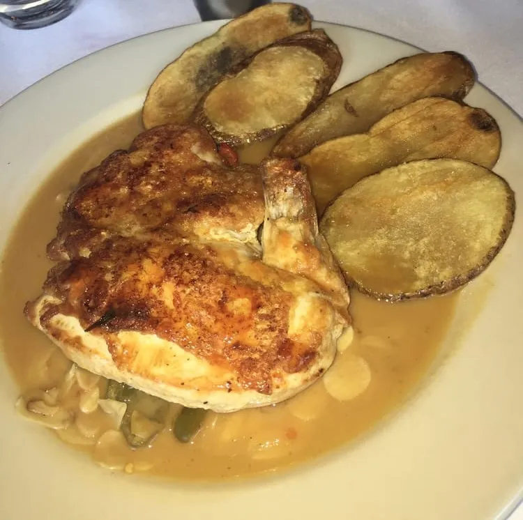 Seared chicken breast in a golden sauce with green peppers, next to roasted potato rounds, at Barcelona Wine Bar