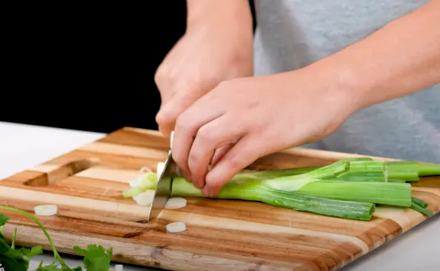 Hands slicing scallions into thin rounds on a wooden board