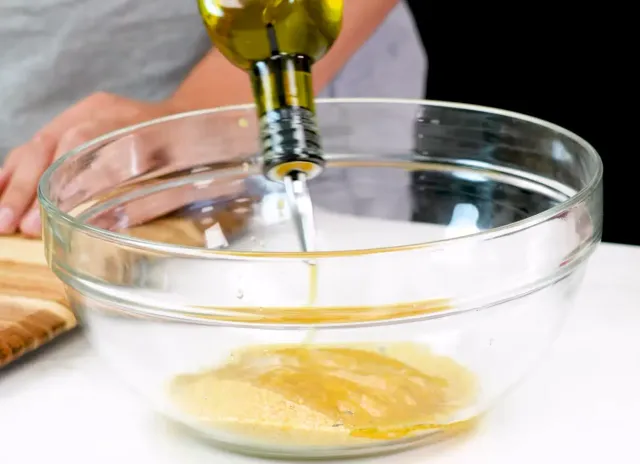 Olive oil pouring from a bottle into a glass bowl of lemon juice and fine bulgur
