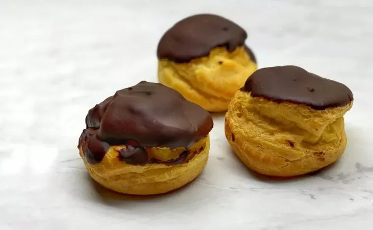 Three round eclairs dipped in chocolate on a marble counter