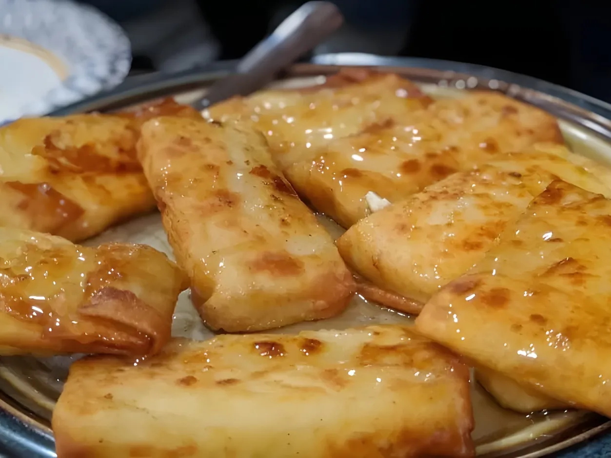 Golden fried feta envelopes in filo, glazed with honey, on a round metal plate