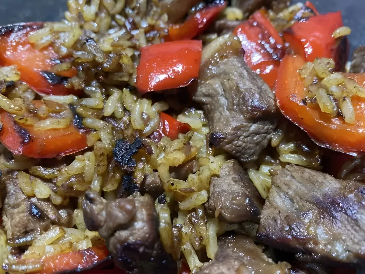 Close-up of fried rice with seared cubes of steak and charred pieces of red bell pepper, the rice browned and crispy in places