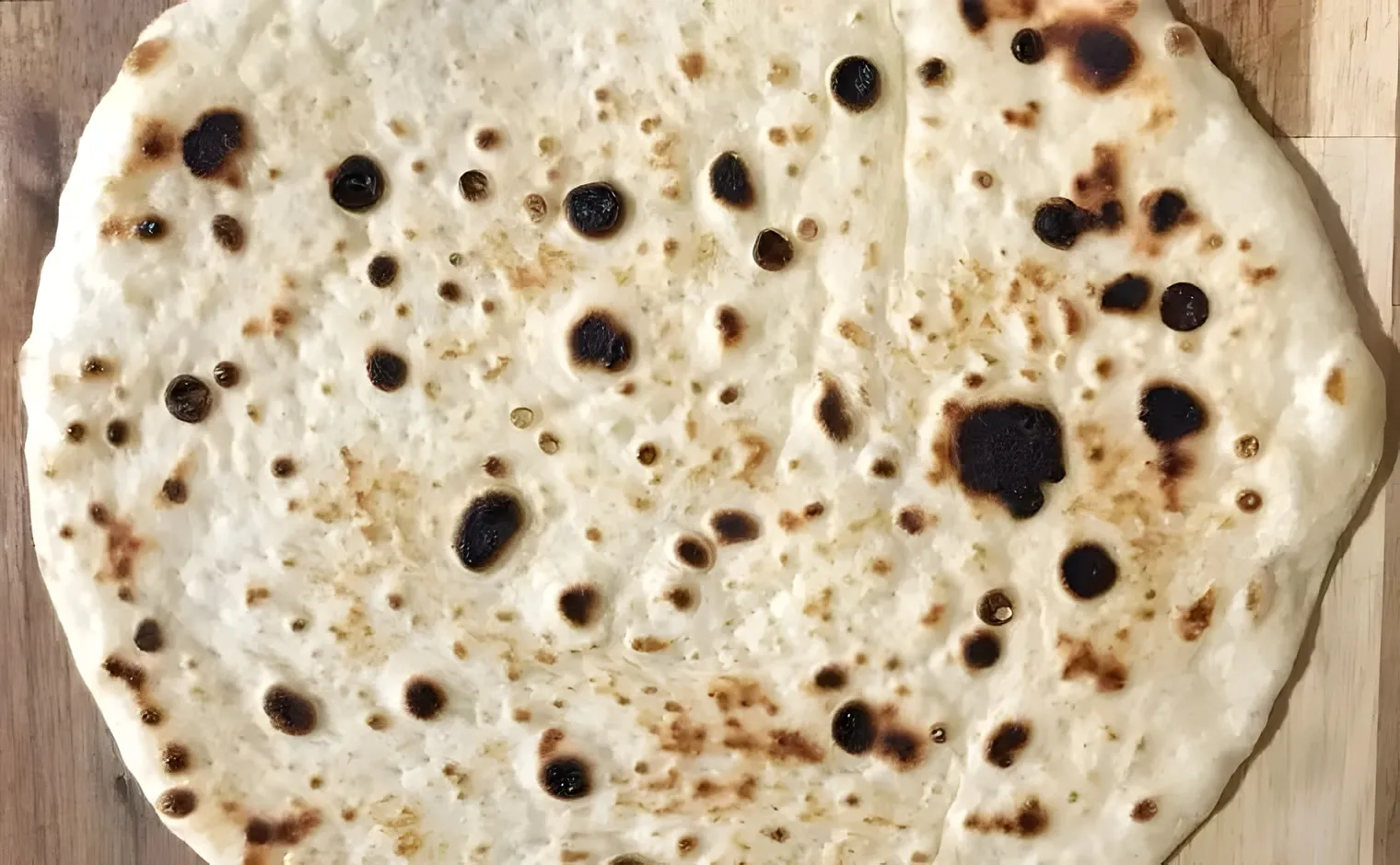 A homemade Greek pita with dark charred spots, on a wooden board