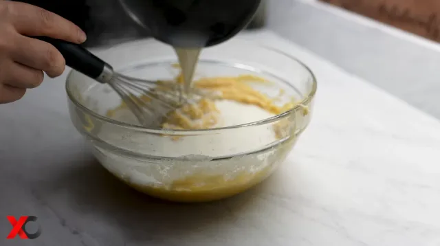 Pouring the warm vanilla milk into the cake batter while whisking
