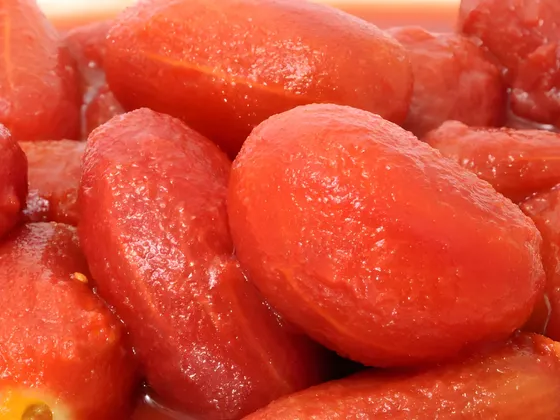 Whole peeled plum tomatoes piled together in their juice, red and glossy with no skin