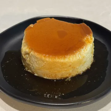 A crème caramel turned out on a black plate, with dark caramel sauce pooled around it