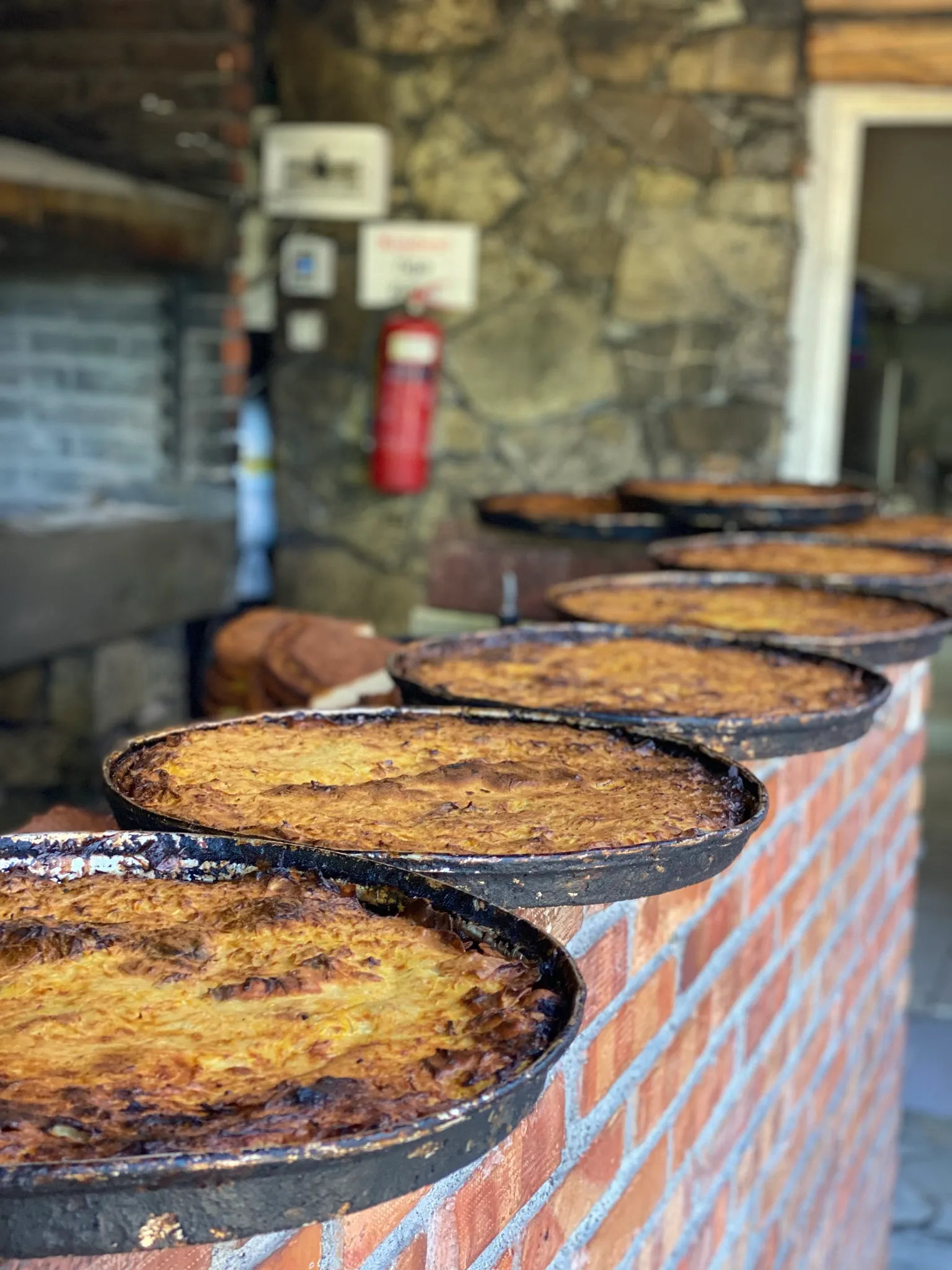 Round pans of freshly baked fli lined up on a brick ledge at Mrizi i Zanave