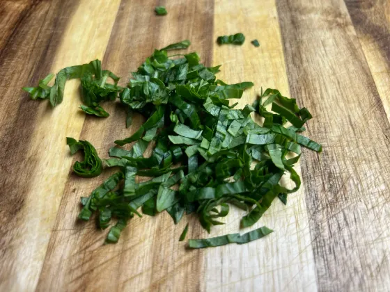 A pile of thin basil ribbons, a basil chiffonade, on a wooden cutting board