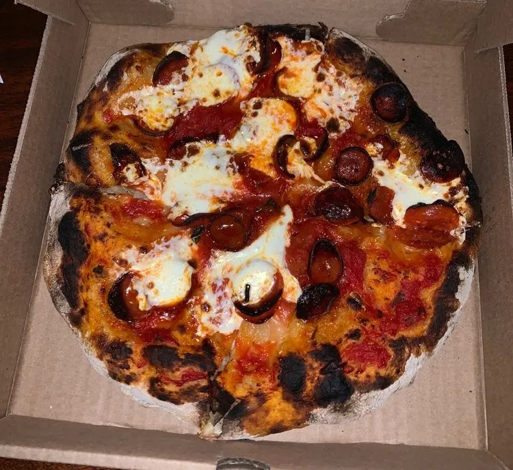 A charred thin-crust pepperoni pizza with tomato sauce and melted mozzarella in an open takeout box, from Picco