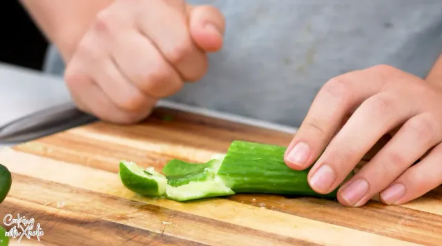 A small cucumber smashed open on a wooden board, between two hands