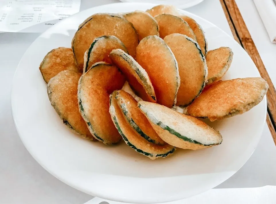 Golden fried zucchini rounds piled on a white plate at KAVA Neo Taverna