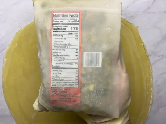 A homemade phyllo sheet laid over a bag of pistachios, thin enough to read the nutrition label through it