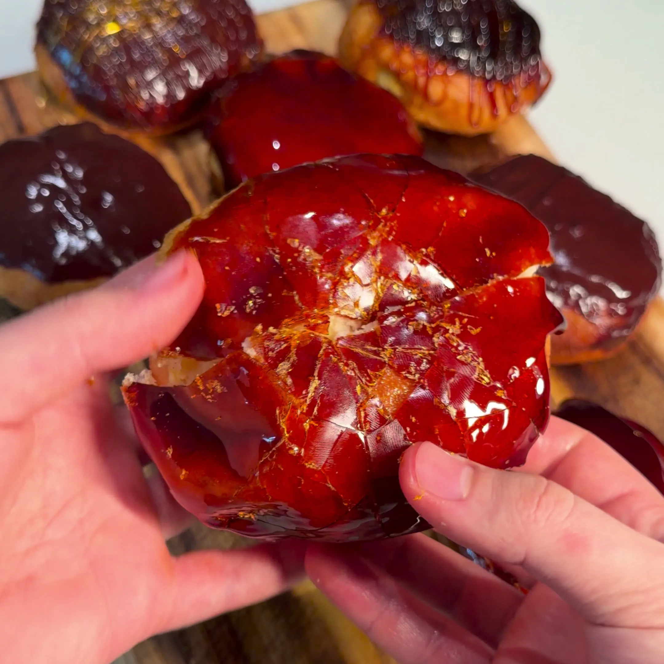 Hands pressing a crème brûlée donut so its caramel top cracks into shards