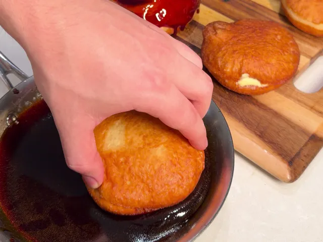 Pressing the top of a filled donut into a skillet of dark caramel