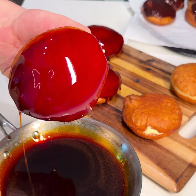 A donut lifted out of the caramel, its top glossy, with a thread of caramel dripping back into the skillet
