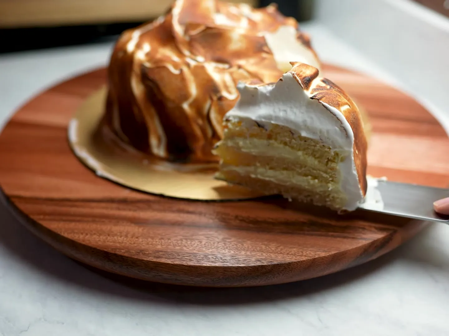 A slice of Cipriani meringue cake lifted out on a knife, showing three cake layers and mascarpone frosting under the torched meringue