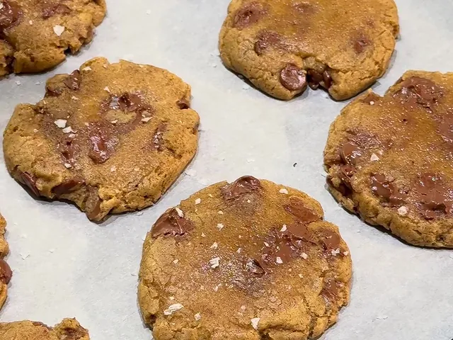Baked chocolate chip cookies with flakes of sea salt on top, on parchment paper