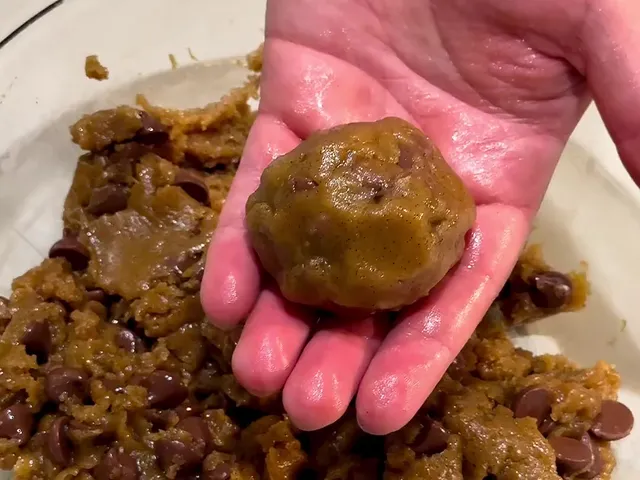 A ball of chocolate chip cookie dough in an open hand, over the bowl of dough