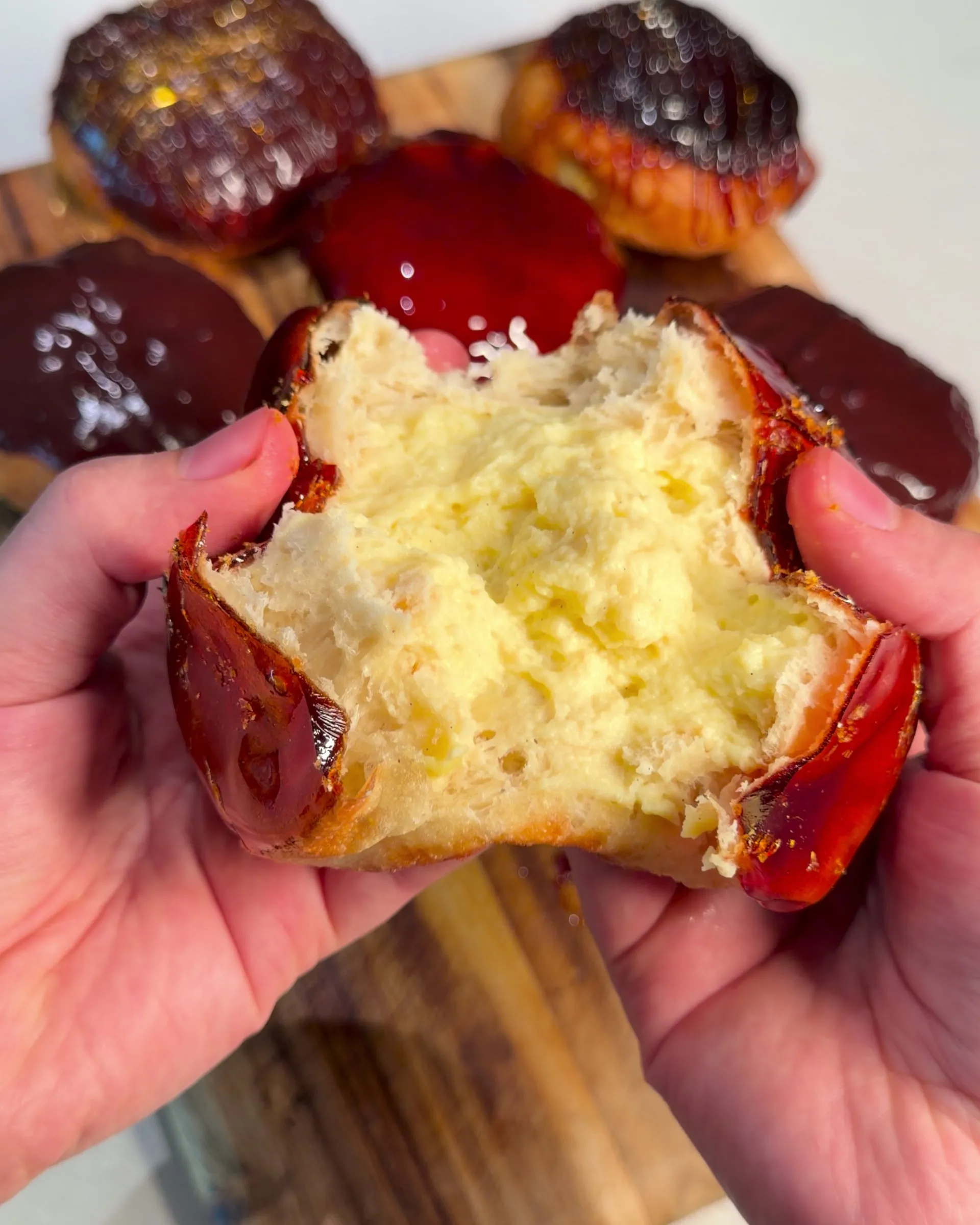Hands pulling a crème brûlée donut open to show the vanilla pastry cream inside, its caramel shell broken at the edges