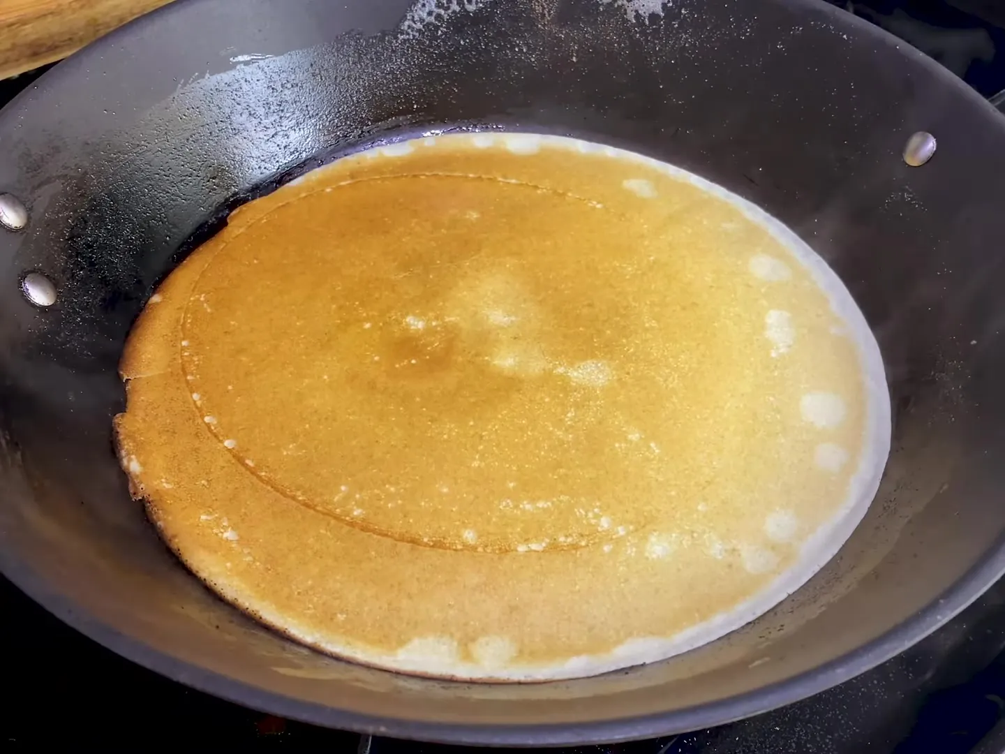 A thin golden crepe cooking in a black pan on the stove