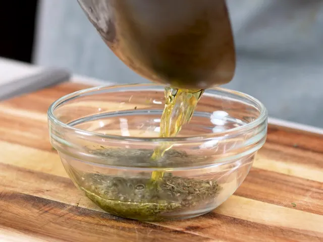 Hot olive oil poured from a pan onto dried mint in a small glass bowl