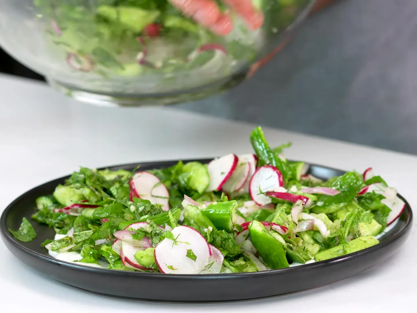 Smashed cucumbers, thin radish slices, red onion, dill and mint piled on Greek yogurt on a black plate