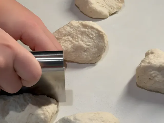 Cutting the byrek dough into pieces with a metal bench scraper on a white counter