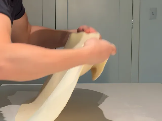 Lifting and pulling the edge of the byrek dough with both hands to stretch it