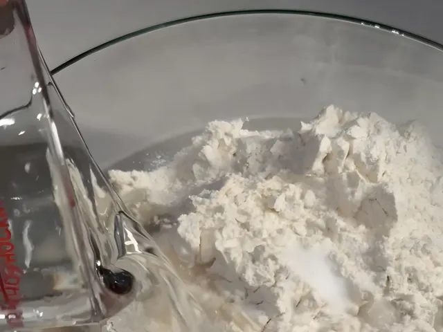 Water pouring from a glass jug into a bowl of flour and salt
