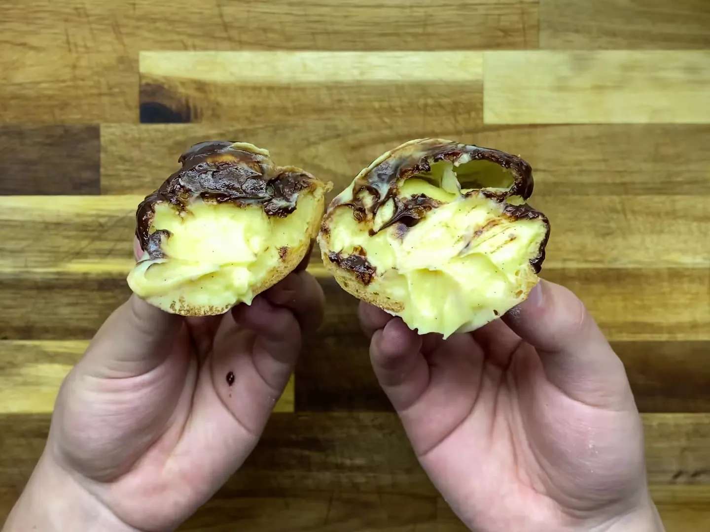 A round chocolate-dipped eclair broken in half to show the vanilla pastry cream inside
