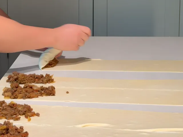 Folding the end of a dough strip over the beef filling on a kitchen island