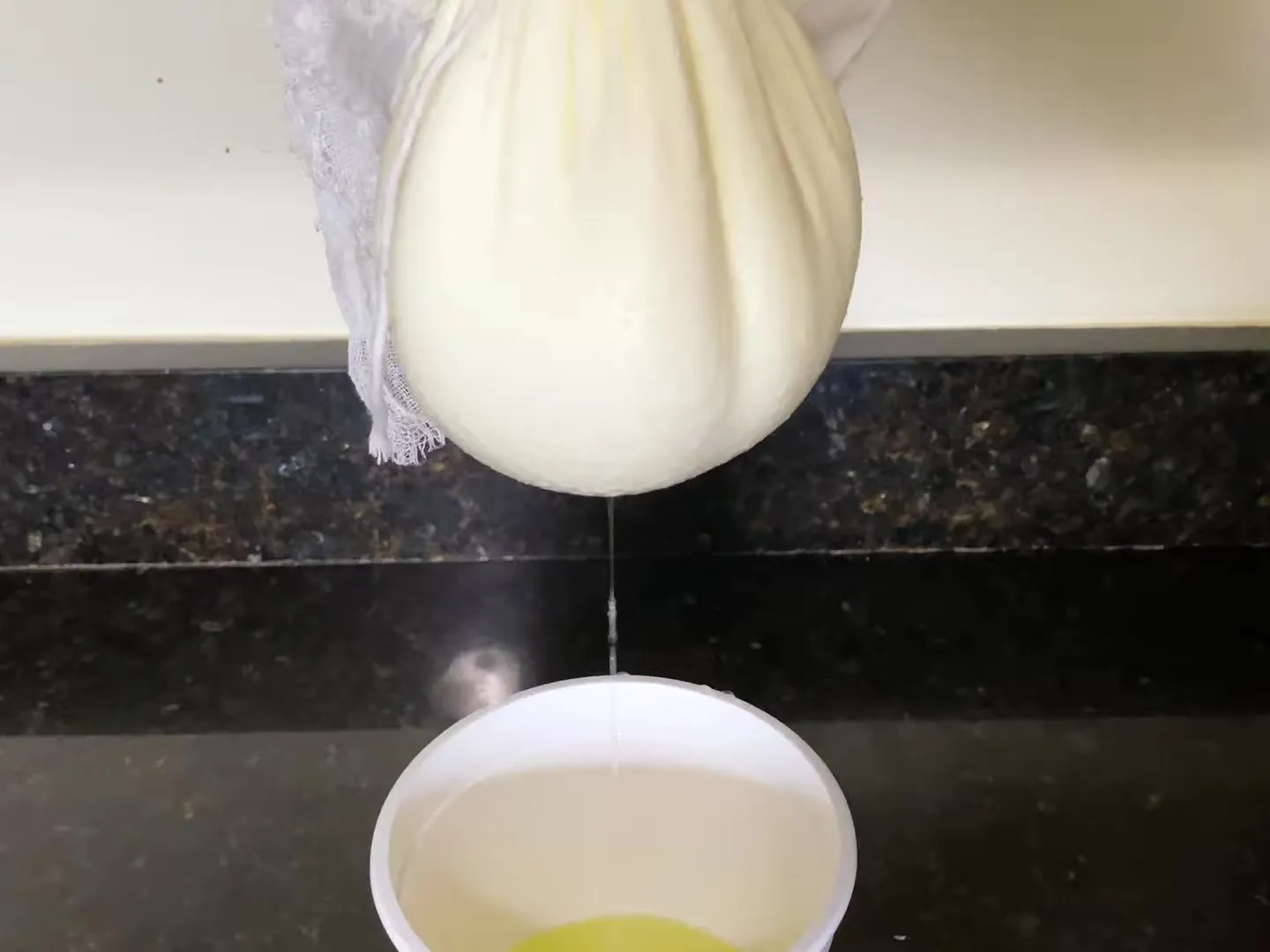 Homemade farmers cheese hanging in a cheesecloth, with the whey dripping into a bucket below