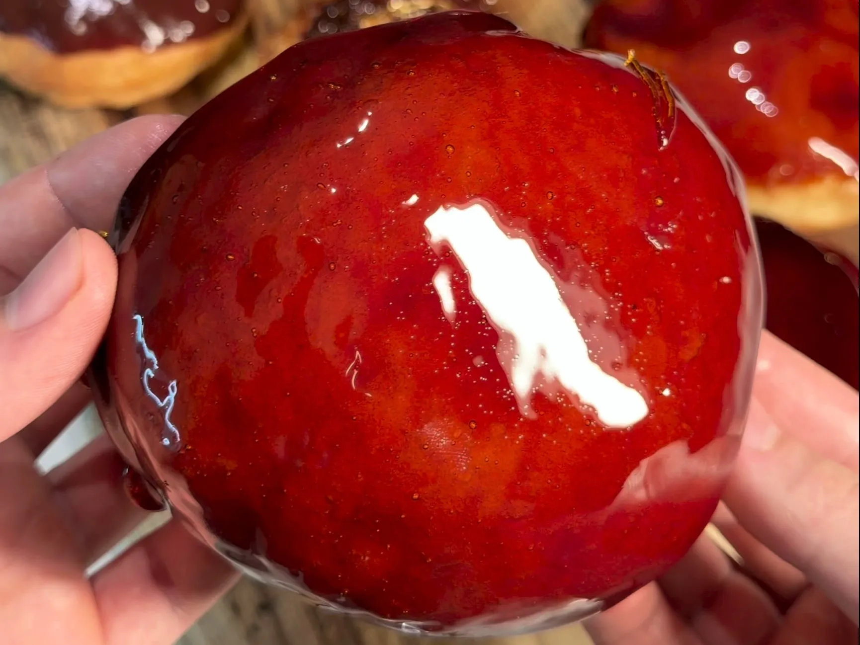 A crème brûlée donut held up in two hands, its glossy caramel top catching the light, over a board of caramel and chocolate donuts