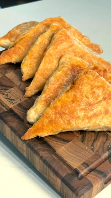 Golden, flaky byrek triangles lined up on a wooden board
