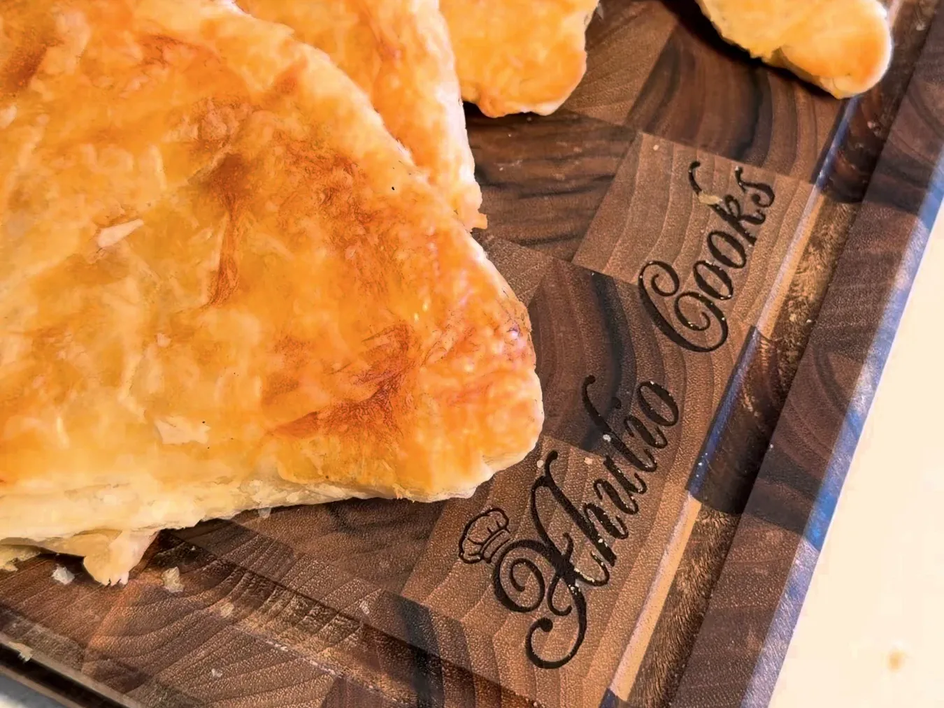Golden, flaky triangles of pumpkin byrek on a wooden board engraved Xhulio Cooks