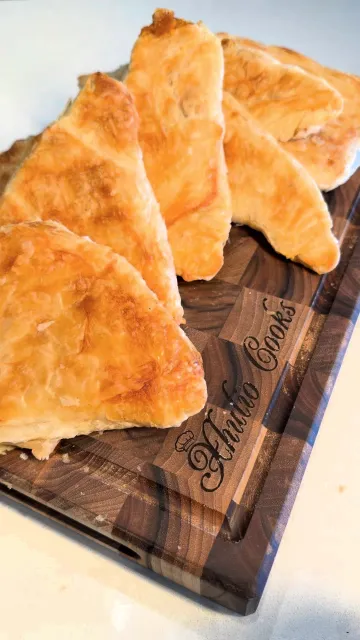 Golden, flaky triangles of pumpkin byrek on a wooden board engraved Xhulio Cooks