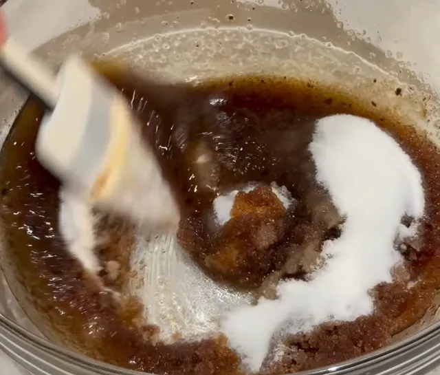 White sugar going into the brown sugar and browned butter in a glass bowl, with a spatula