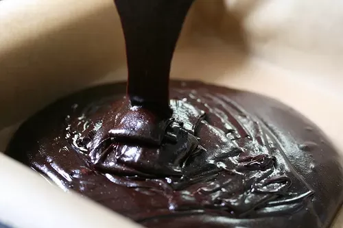 Thick, glossy chocolate batter pouring into a pan lined with parchment paper