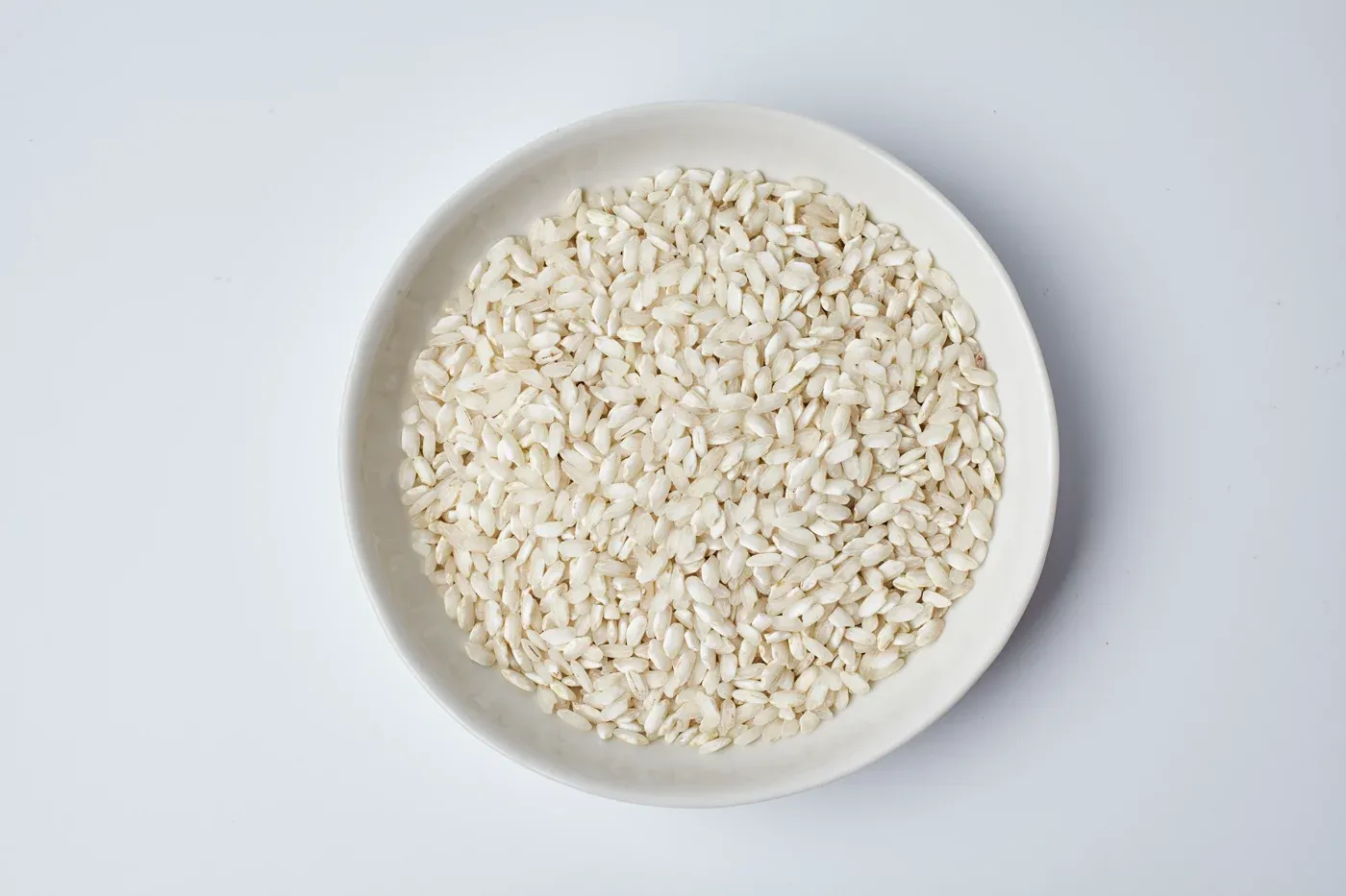 A white bowl of uncooked risotto rice, seen from above