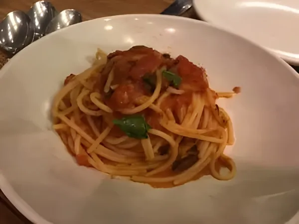 Spaghetti al pomodoro with chunks of tomato and a few basil leaves in a white bowl