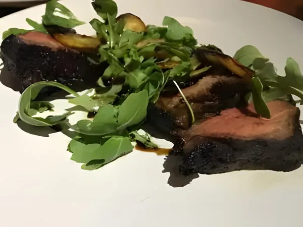 Slices of grilled steak, charred outside and pink inside, with arugula on a white plate