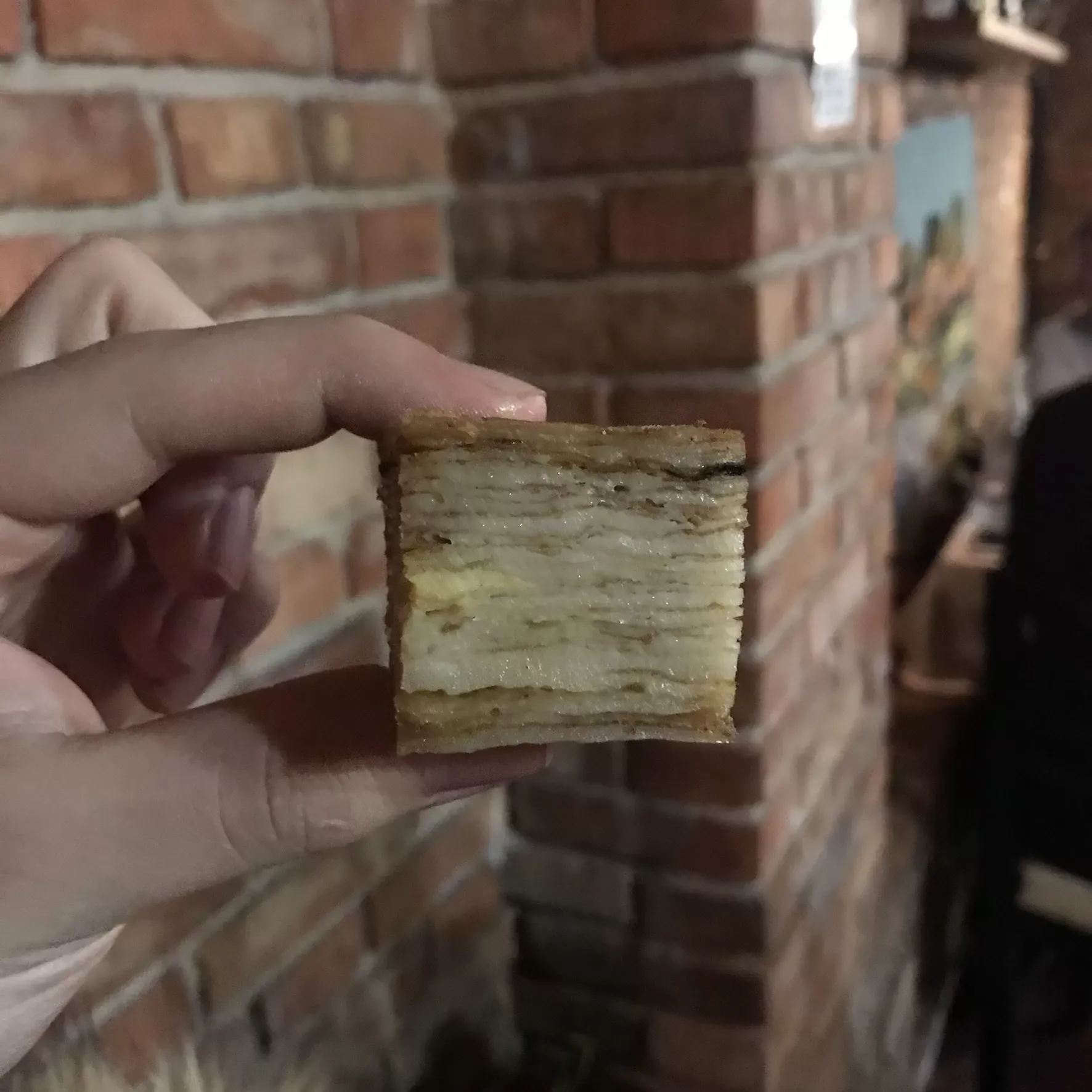 A hand holding up a slice of fli to show its thin baked layers