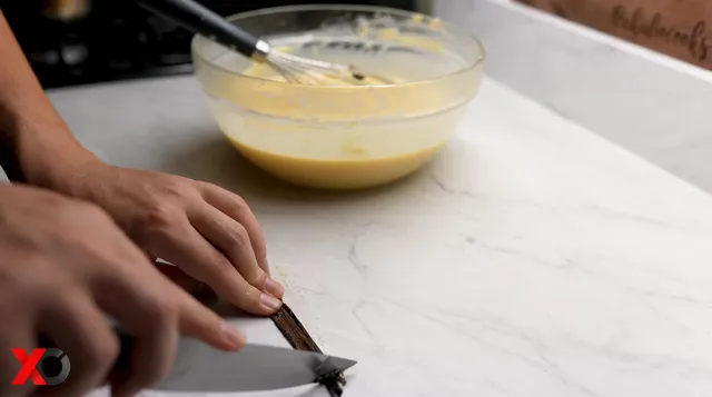 Scraping the seeds out of a split vanilla bean with a knife