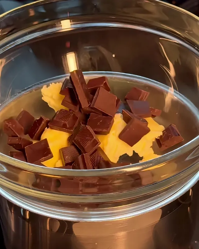 Pieces of chocolate and soft butter in a glass bowl set over a steel pot, before they melt