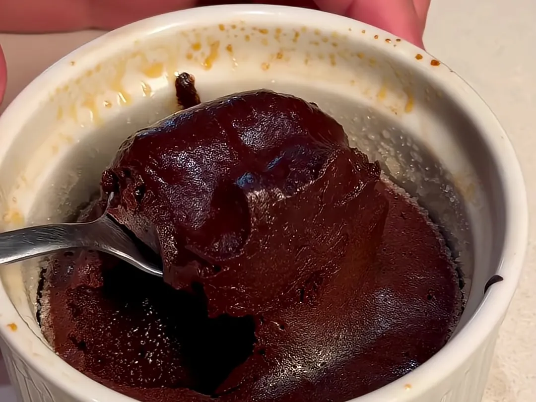 A baked lava cake in a white ramekin, with a spoon lifting out the soft, runny middle