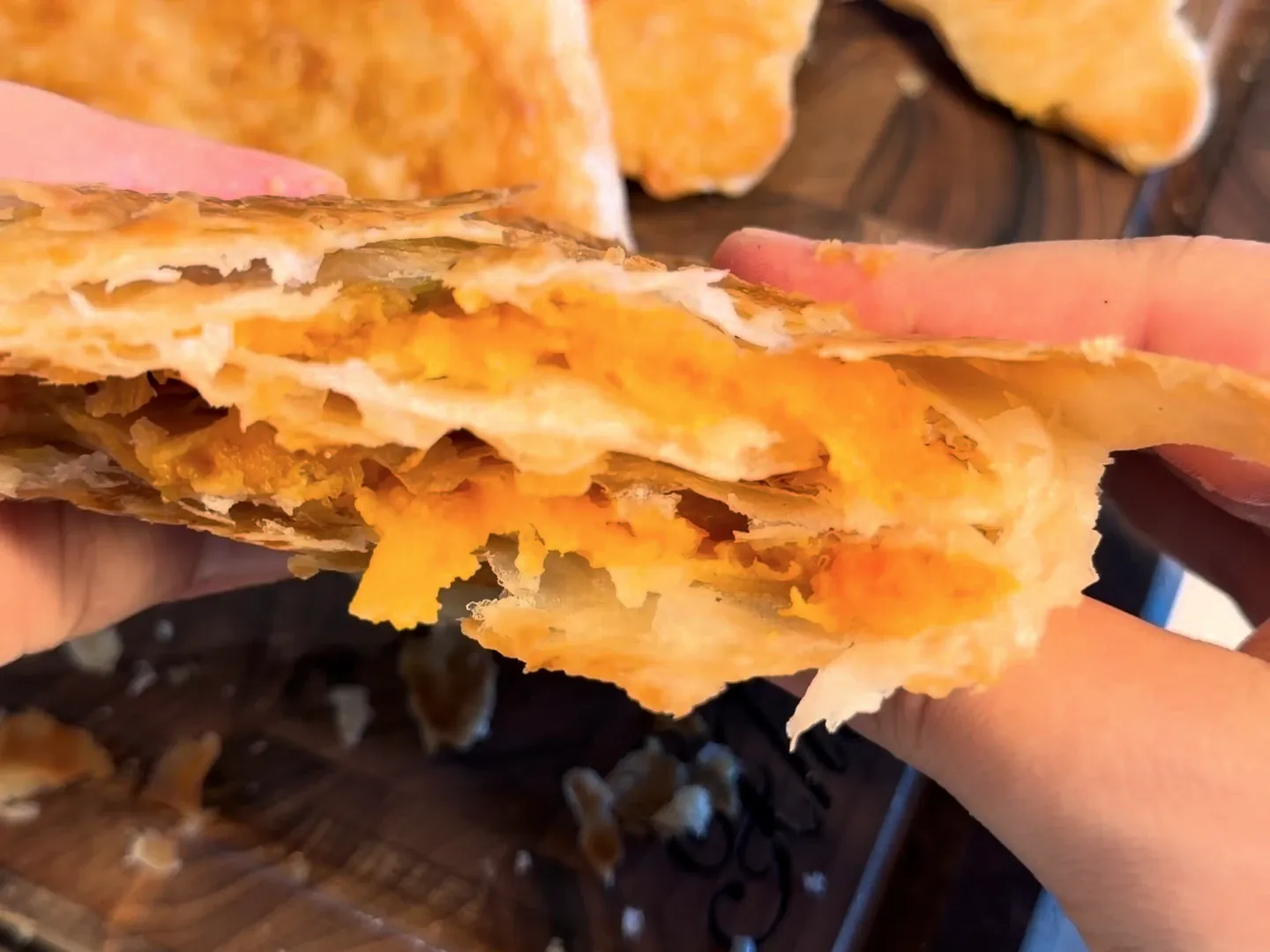 Two hands pulling a baked byrek triangle apart, showing the thin layers and the orange pumpkin filling inside