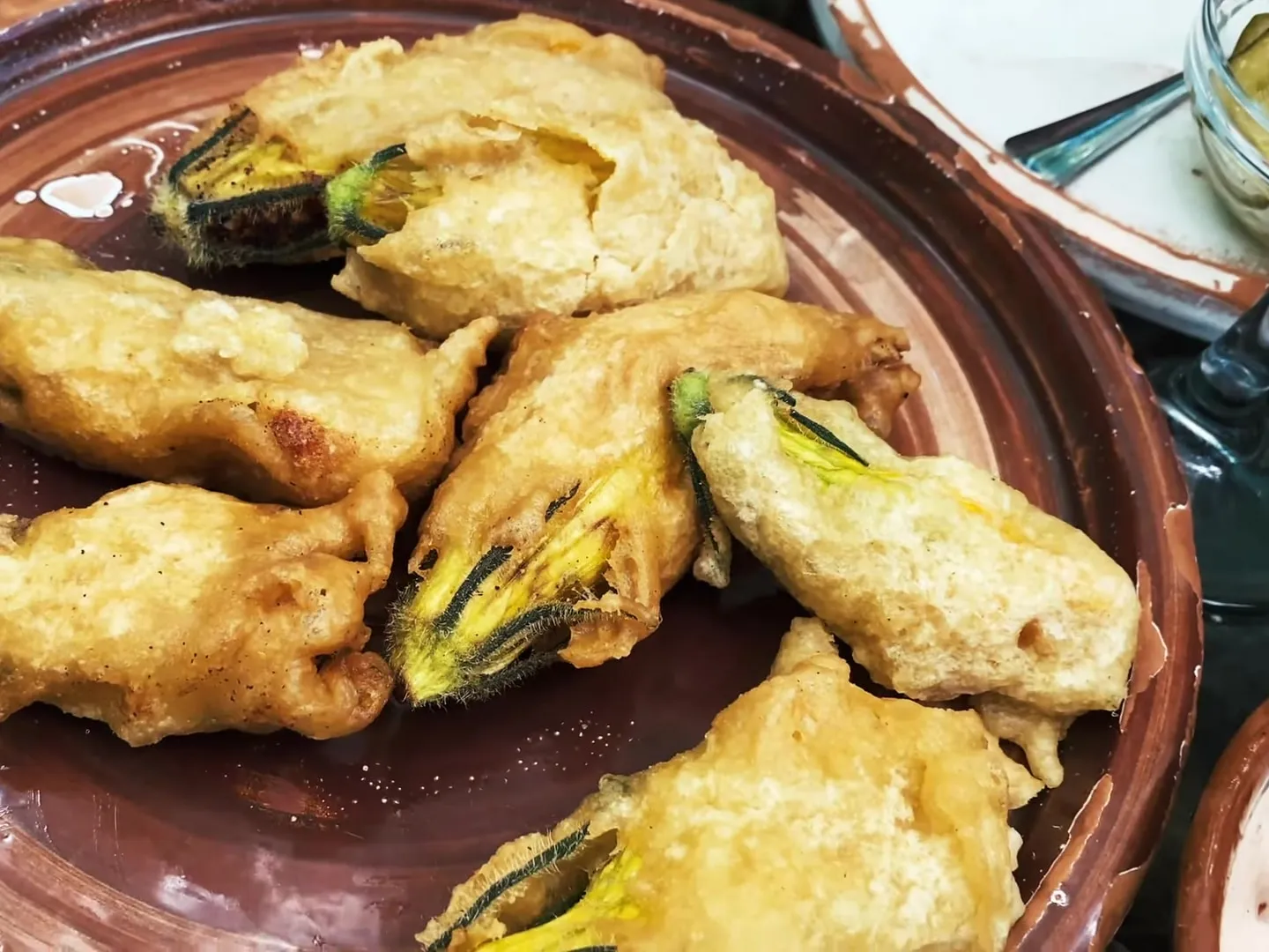 Battered and fried stuffed zucchini blossoms on a brown clay plate at Mrizi i Zanave